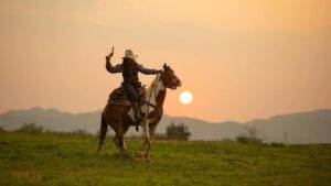 36528170 Cowboy Riding Horse Against Sunset E1680617233367 300x169 